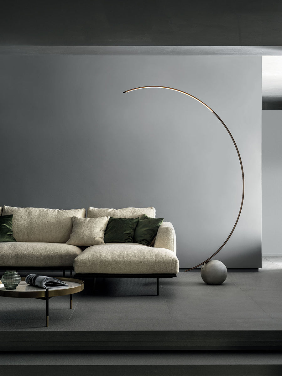 Elliptical modern Circle metal floor lamp done in dark brass with concrete ball base. Placed in a living room.