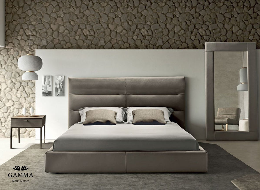 Sayonara leather bed in light colors with high headboard, front view, placed in a modern room with a side table, a mirror, and a chair.
