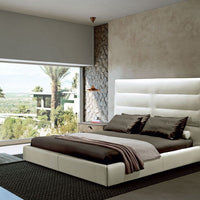 Sayonara leather bed in light colors with high headboard, placed with side tables in a modern room with a great view.