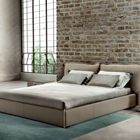 King Size Leather bed in grey color with a soft headboard, placed in a bricked wall room.