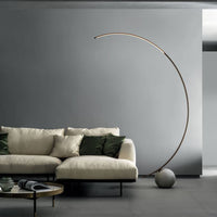 Elliptical modern Circle metal floor lamp done in dark brass with concrete ball base. Placed in a living room.