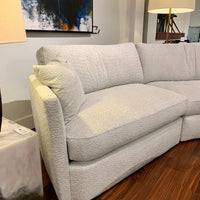 White fabric No Right Angles Sectional with curved lines on the front, sides and back. Partial view. Placed in a furniture store.