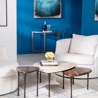 Three different sized Reuleaux Drink Tables placed in front of a white chair and with a vase and books on one of them.