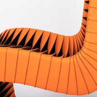 Orange and black Seat Belt dining chair with colorful seatbelt strappings, closed up side view.