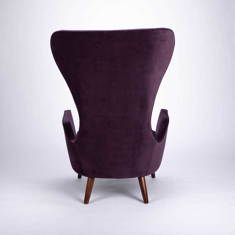 A purple Granta lounge chair with exaggerated curves and period style legs and arms. Back view.