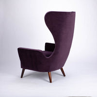 A purple Granta lounge chair with exaggerated curves and period style legs and arms. Side view.