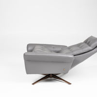 A grey leather recliner chair with buttonless tufted back and seat and four star base, side view, reclined.