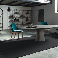 Podium Dining Table with concrete oval base and matching round top. Placed in a room with three blue dining chairs.