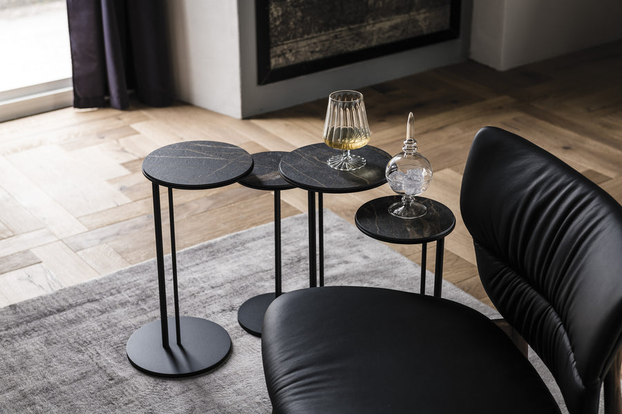 Collection of four black side tables with a drink on one of them and an ice on other. Placed beside a black chair.
