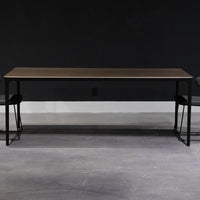 Slim Dining Table with die cast aluminum legs and wooden top. Placed in a room with two black dining chairs.