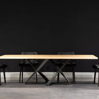 Millennium Oak Dining Table with the solid natural oak top and classic metal base design. Placed in a room with four black leather dining chairs.