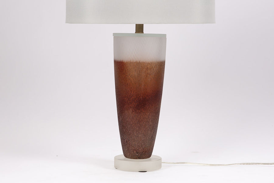 Two-toned Caledonia Table Lamp with an urn shaped form on an opaque lucite base and a white shade. Closed up view on the base and partial view of the shade.