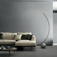 Elliptical modern Circle metal floor lamp done in dark brass with concrete ball base. Placed in a living room.