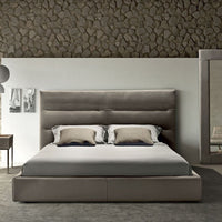 Sayonara leather bed in light colors with high headboard, front view, placed in a modern room with a side table, a mirror, and a chair.
