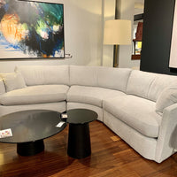 White fabric No Right Angles Sectional with curved lines on the front, sides and back. Placed in a furniture store.