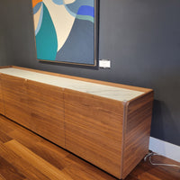 Pica Cabinet in Walnut Finish with four doors and four compartments and white top panel. Side view in a room with purple wall.