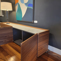 Pica Cabinet in Walnut Finish with four doors and four compartments and white top panel. Side view in a room with purple wall. Two doors are opened, showing inside compartments.