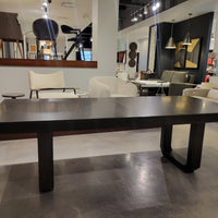 Oliver Dining Table with chamfered solid Ash base and strong top in dark walnut finish. Placed in a furniture store.