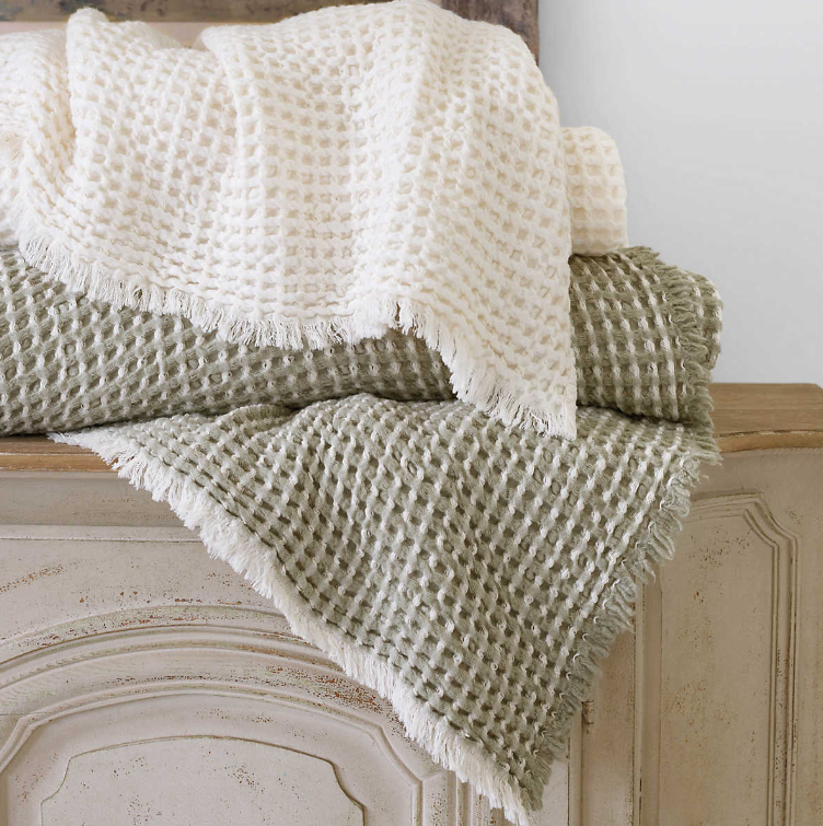 A white and a green King size Dorothy Sage Blanket In a blend of cotton and soft wool, placed on a dresser.