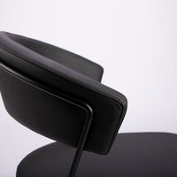 A black leather New York Dining Chair with metal frame and sled base and curved back. Closed up top view.