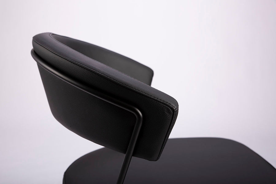 A black leather New York Dining Chair with metal frame and sled base and curved back. Closed up top view.
