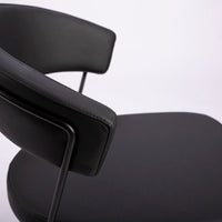 A black leather New York Dining Chair with metal frame and sled base and curved back. Closed up side view.