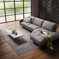Grey leather Glamour sectional with a special design where the seat and backrest cushions are rested on a linear frame offering a sartorial arm detail. Placed in a modern living room.
