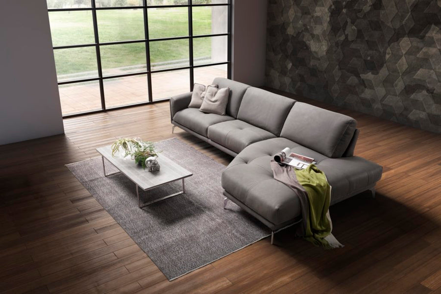 Grey leather Glamour sectional with a special design where the seat and backrest cushions are rested on a linear frame offering a sartorial arm detail. Placed in a modern living room.