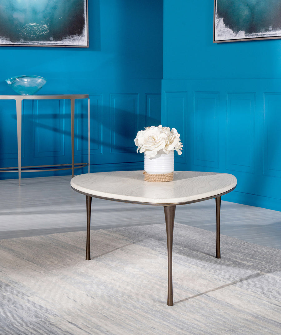Reuleaux Large Cocktail Table with rounded, asymmetrical top and elegantly tapered legs, with a vase and flowers on it, placed in a room with blue walls.