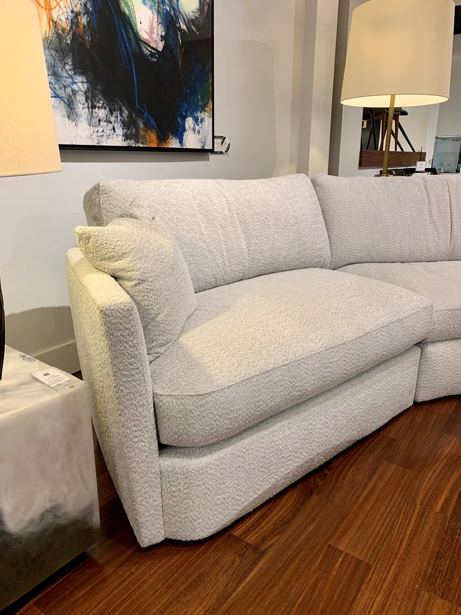 White fabric No Right Angles Sectional with curved lines on the front, sides and back. Partial view. Placed in a furniture store.