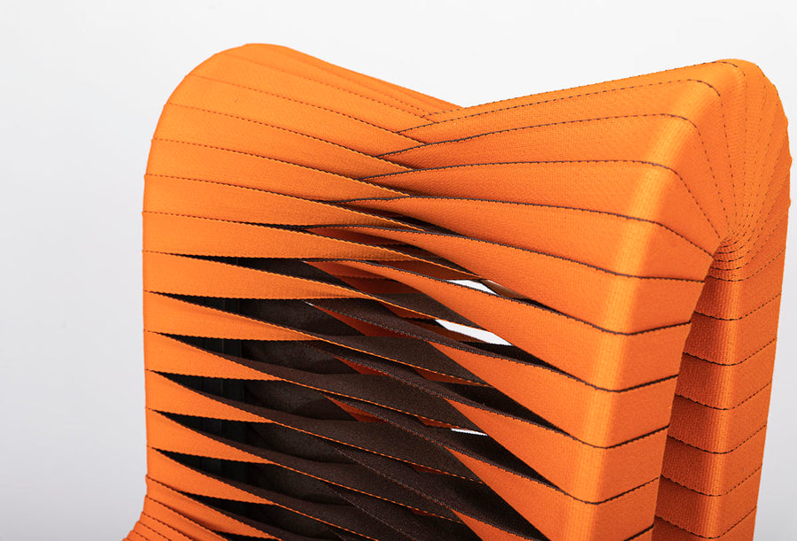 Orange and black Seat Belt dining chair with colorful seatbelt strappings, closed up top view.