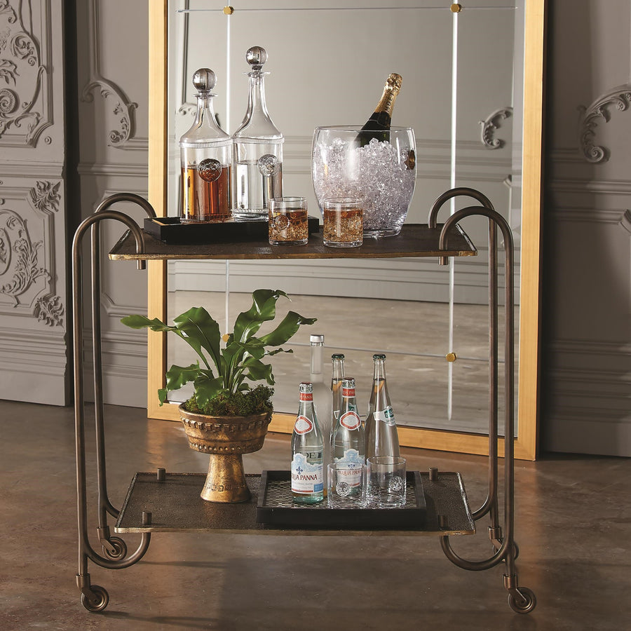 Two level Blade Bar Cart with cast textured aluminum bronze finished upper and lower shelves separated and held in place with four arching hollow iron tubing legs. Drinks are placed on both shelves.