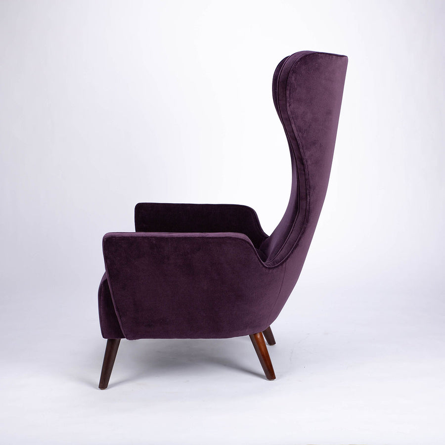 A purple Granta lounge chair with exaggerated curves and period style legs and arms. Side view.