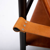 Pipe lounge chair with thick saddle leather strapped to striking metal frame, closed up side view.