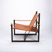 Pipe lounge chair with thick saddle leather strapped to striking metal frame, side view.