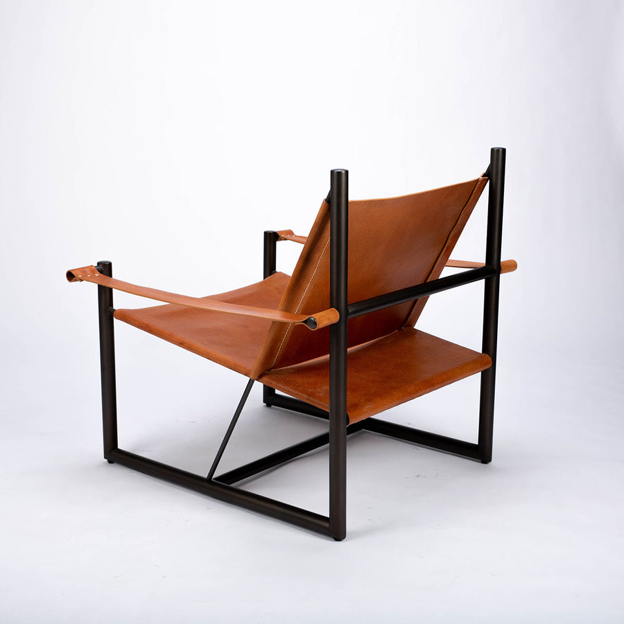 Pipe lounge chair with thick saddle leather strapped to striking metal frame, side and back view.
