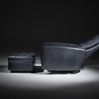 A blue Lanier leather recliner chair with the shape of classic automotive designs, reclined and with ottoman, side view.