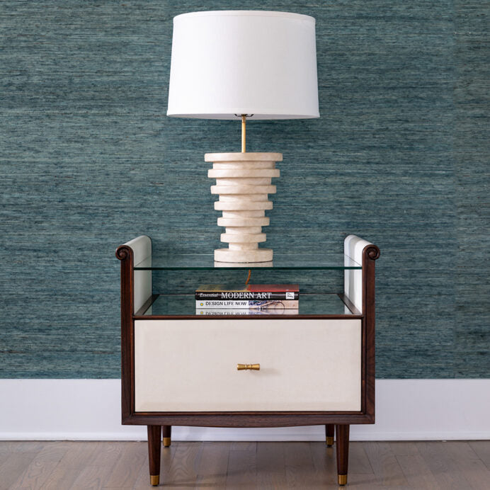 Hepburn Bedside with a lamp on top and books - single drawered Vellum clad bedside table with Rosewood legs and Aged Brass detail. Has a top with scrolled sides, which supports a toughened glass top that rests above an Verre Eglomise insert.