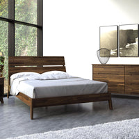 Linn queen size bed crafted from reclaimed walnut hardwood with contemporary design, side view, with bedside table, placed in a well light room.