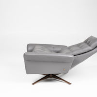 A grey leather recliner chair with buttonless tufted back and seat and four star base, side view, reclined.
