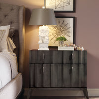Ava Hall chest, black, placed beside a bed and with lamp, plant and books on it.