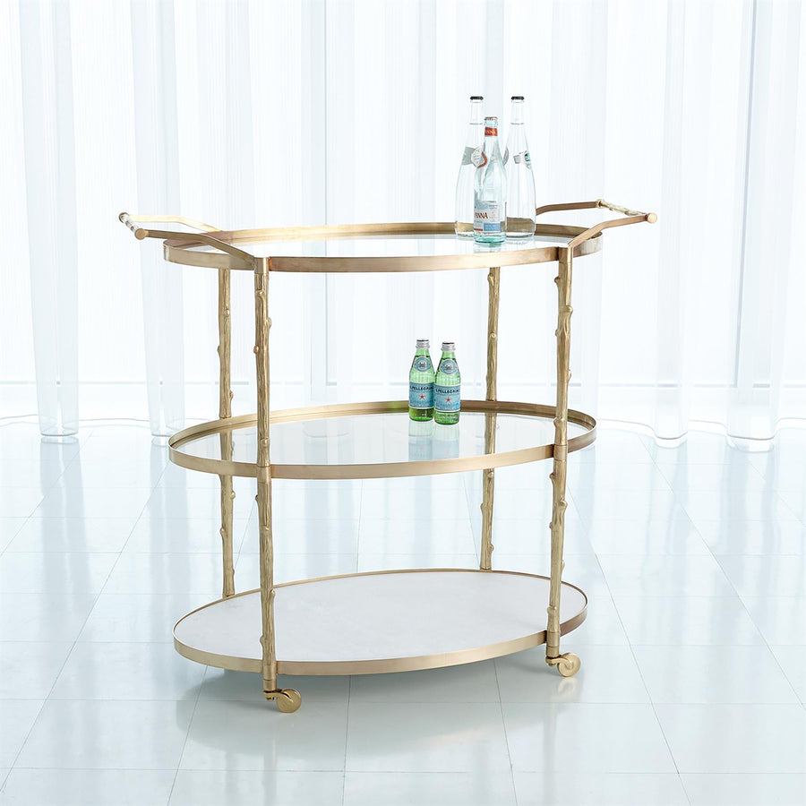 Arbor 3 level Bar Cart with twig textured detailing on the supports and handles, a solid white marble bottom shelf, and two glass upper shelves with solid brass pivoting wheels.