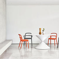 Fixed round Clessidra Dining Table with white base and white top. Placed in a white room with two orange chairs and two black chairs.
