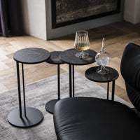 Collection of four black side tables with a drink on one of them and an ice on other. Placed beside a black chair.