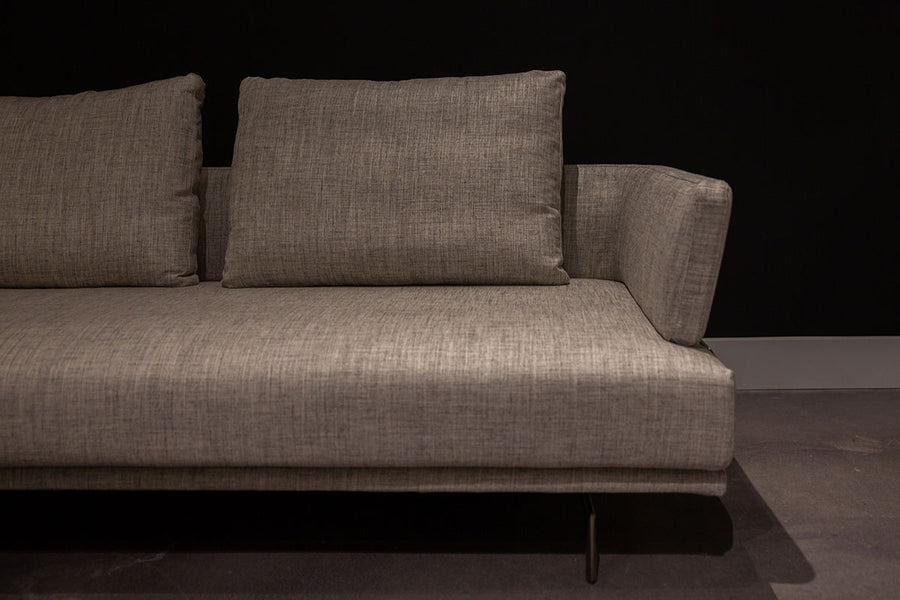 Light grey Quinta Strada Sectional with black chrome finish of the feet, the thinner joining clamps, and light base and back support. Partial left view.