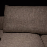 Light grey Quinta Strada Sectional with black chrome finish of the feet, the thinner joining clamps, and light base and back support. Closed up view of a pillow. 