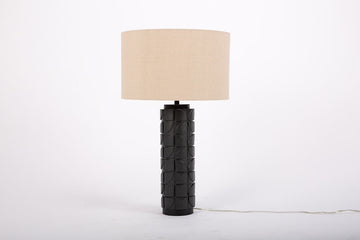 Mimi lamp with a beige linen shade and mate-black body with dimensional carving pattern.