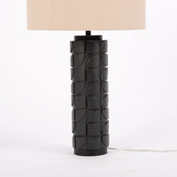 Mimi lamp with a beige linen shade and mate-black body with dimensional carving pattern. Closed up view on the body.