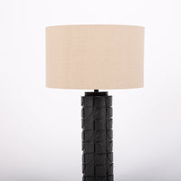 Mimi lamp with a beige linen shade and mate-black body with dimensional carving pattern. Closed up view on the body and the shade.