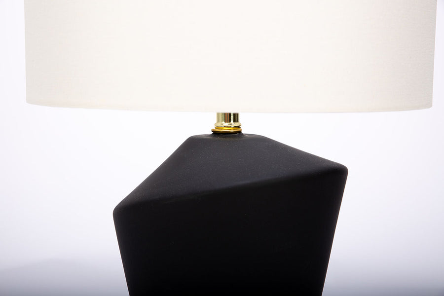 Gavin table lamp with a drum white shade and modern black ceramic body in an unique asymmetric design and a contrasting gold base. Closed up partial view of the body and the shade.